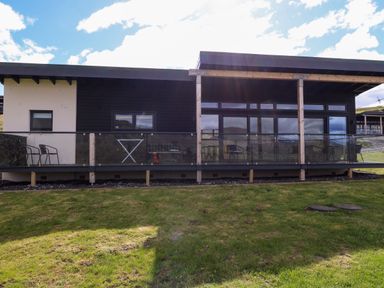 A modern single-story building with a glass balcony railing and outdoor chairs at 2 Strathtay Lodges in Aberfeldy