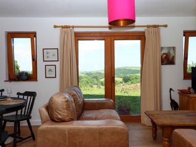 A living room with a brown leather sofa wooden coffee table and double glass doors showing a green landscape at South Holm in Moreleigh