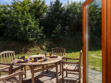 A wooden patio table with plates and glasses set for breakfast on a garden patio at South Holm in Moreleigh