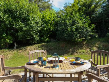 A wooden round table with breakfast items and wooden chairs in a garden with trees at South Holm in Moreleigh