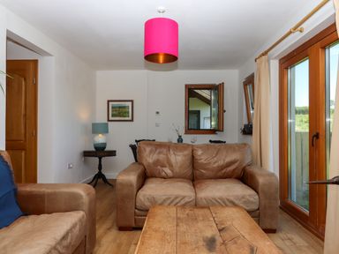 A living room with brown leather sofas wooden coffee table side table with lamp framed picture on wall and large windows at South Holm in Moreleigh
