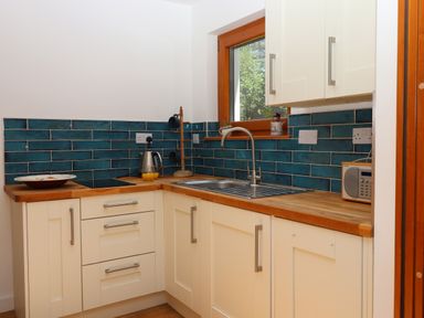 A kitchen with wooden countertops white cabinets a stainless steel sink a window blue tiled backsplash and a kettle with orange juice on the counter at South Holm in Moreleigh