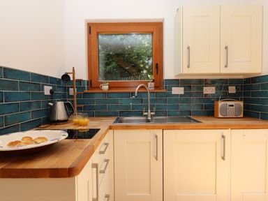 A kitchen with wooden countertops white cabinets blue tiled backsplash and a window at South Holm in Moreleigh