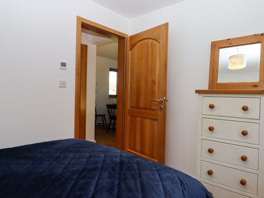 A bedroom with a wooden door open showing a dining area and a white dresser with a mirror at South Holm in Moreleigh