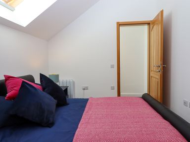 A bedroom with a bed featuring navy and pink bedding a bedside table with a lamp and an open wooden door at South Holm in Moreleigh