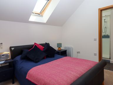 A bedroom with a bed with dark blue bedding and pink blanket with bedside tables and a skylight at South Holm in Moreleigh