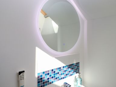 A bathroom mirror above a sink with blue and purple tiles on the wall at South Holm in Moreleigh