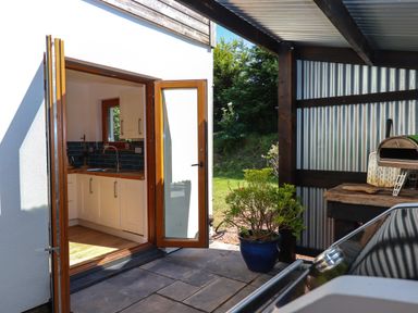 An open door leading from a kitchen to an outdoor area with a potted plant and a covered space with a wood-fired oven