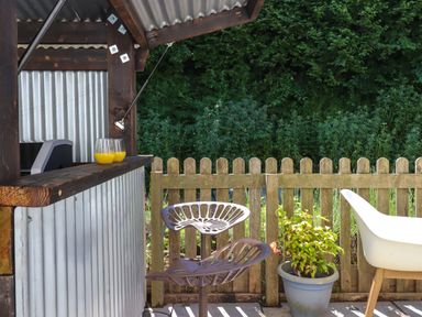 An outdoor seating area with metal stools a wooden fence and a potted plant at South Holm in Moreleigh