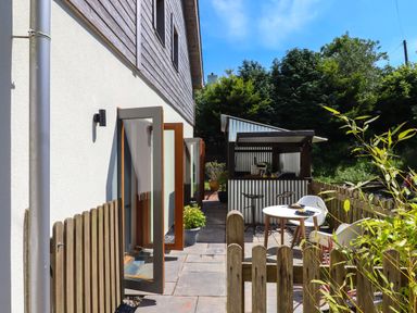 An outdoor patio area with a small wooden fence a round table with chairs and a corrugated metal and wood bar at South Holm in Moreleigh