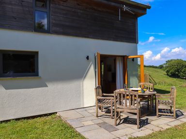 An outdoor patio with a wooden table and four chairs outside a house at South Holm in Moreleigh
