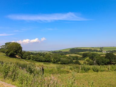 A countryside landscape with green fields trees and hills under a blue sky at South Holm in Moreleigh