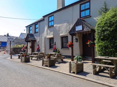 An outdoor seating area with wooden picnic tables and umbrellas outside a building with hanging flower pots at The New Inn in Moreleigh
