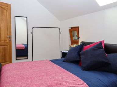 A bedroom with a bed dressed in blue and pink bedding next to a wooden door and a tall mirror on the wall at South Holm in Moreleigh