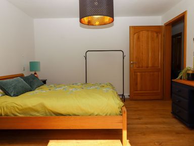 A bedroom with a wooden bed with green and floral bedding a wooden door a black dresser a clothes rack and a lamp at South Holm in Moreleigh