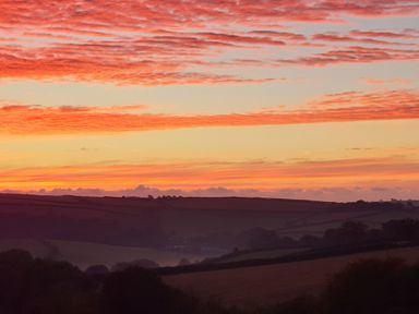 A landscape of fields and hills under a sky with orange and pink clouds at sunset at South Holm Moreleigh