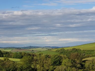 A landscape with rolling green hills and trees under a partly cloudy sky at South Holm in Moreleigh