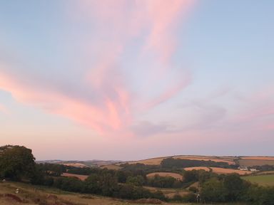 A rural landscape with fields trees and hills under a sky with pink clouds at South Holm in Moreleigh