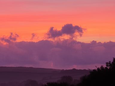 A landscape with hills and trees under a sunset sky with orange and purple clouds at South Holm in Moreleigh