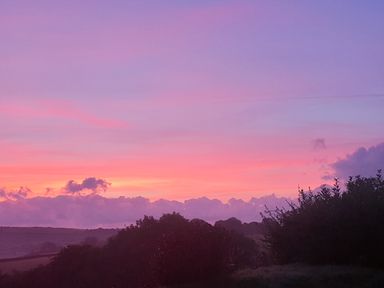A landscape with trees and hills under a colorful sunset sky at South Holm in Moreleigh
