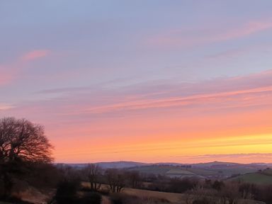 A landscape with rolling hills and bare trees under a colorful sunset sky at South Holm in Moreleigh