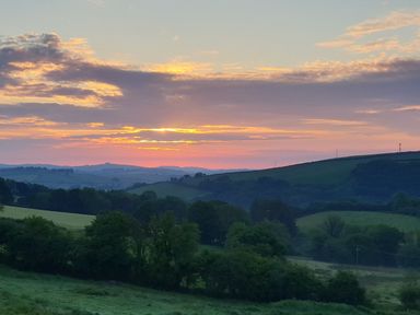 A countryside landscape with rolling hills and trees under a sunset sky at South Holm in Moreleigh