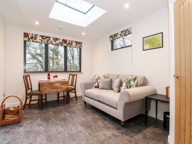 A sitting area with a sofa and small dining table with two chairs near windows at Herdwick Cabin in Hutton John near Penruddock