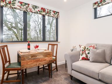 A small dining table with two chairs near windows and a gray sofa with floral cushions at Herdwick Cabin in Hutton John near Penruddock
