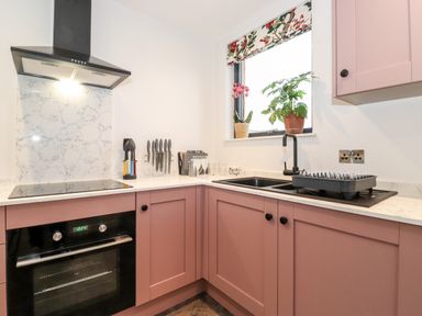 A kitchen with pink cabinets a black oven a black sink a drying rack and plants on the windowsill at Herdwick Cabin in Hutton John near Penruddock