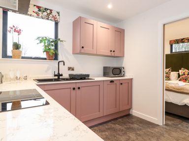A kitchen with pink cabinets a black sink a microwave and plants on the windowsill at Herdwick Cabin in Hutton John near Penruddock