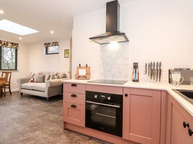 A kitchen with pink cabinets a black oven and stovetop a sofa by the window at Herdwick Cabin in Hutton John near Penruddock