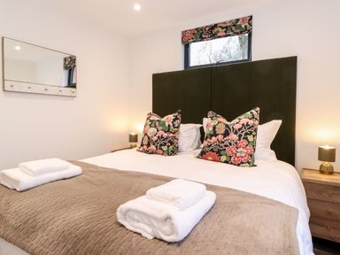 A bedroom with a double bed with floral pillows and towels on a beige blanket Herdwick Cabin in Hutton John near Penruddock