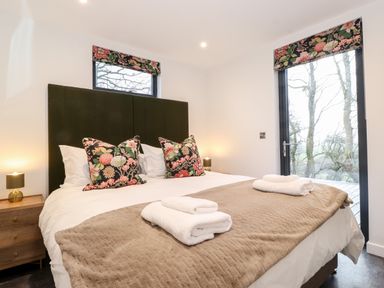 A bedroom with a bed with floral pillows and folded towels at Herdwick Cabin in Hutton John near Penruddock