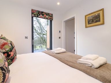 A bedroom with a bed having floral pillows and folded towels on a brown runner next to a door with a floral window shade at Herdwick Cabin in Hutton John near Penruddock