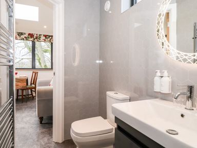 A bathroom with a toilet sink and illuminated mirror next to a dining area with a table and chairs at Herdwick Cabin in Hutton John near Penruddock