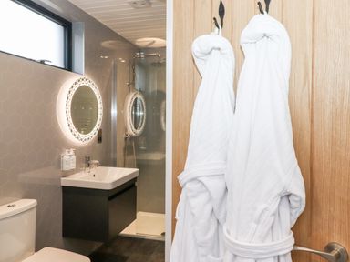 A bathroom with two white bathrobes hanging on a wooden door a toilet a sink with a mirror and a shower at Herdwick Cabin in Hutton John near Penruddock