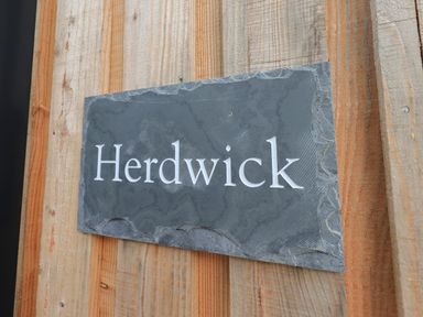 A black stone plaque with the word Herdwick mounted on a wooden wall at Herdwick Cabin in Hutton John near Penruddock