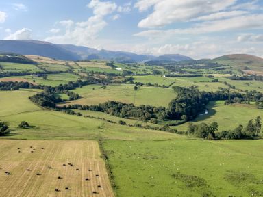Aerial view of green fields and hills with scattered trees and hay bales at Herdwick Cabin in Hutton John near Penruddock