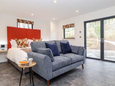A bedroom with a red headboard bed a blue sofa and glass doors showing a garden at The Gardener's Retreat in Hutton John near Penruddock