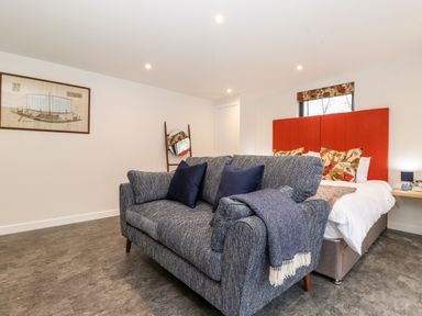 A bedroom with a grey sofa blue cushions a bed with an orange headboard floral pillows and a wall painting at The Gardener's Retreat in Hutton John near Penruddock