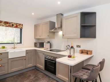 A kitchen with cabinets an oven a sink a microwave and two stools at The Gardener's Retreat in Hutton John near Penruddock