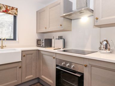A kitchen with a sink microwave oven stovetop kettle and cabinets at The Gardener's Retreat in Hutton John near Penruddock