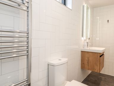 A bathroom with a toilet wooden sink cabinet illuminated mirror and chrome towel radiator at The Gardener's Retreat in Hutton John near Penruddock