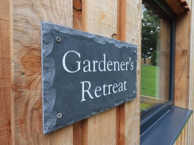 A wooden wall with a slate sign reading Gardeners Retreat beside a window at The Gardeners Retreat in Hutton John near Penruddock