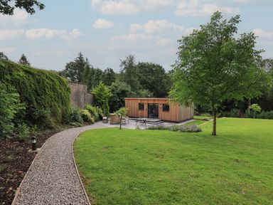 A garden with a gravel path leading to a wooden cabin surrounded by trees and grass at The Gardener's Retreat in Hutton John near Penruddock
