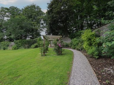 A garden with a gravel path curved along a flower bed and a wooden pergola at The Gardener's Retreat in Hutton John near Penruddock