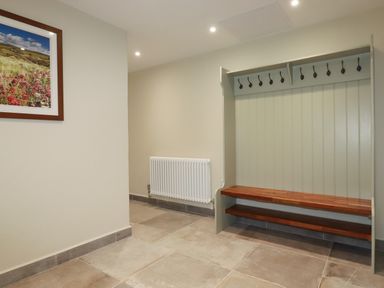 A hallway with a white radiator a bench with hooks and a framed landscape photograph at Tretoil Farm House in Bodmin