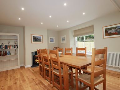 A dining room with a long wooden table and chairs a bookshelf and a fireplace at Tretoil Farm House in Bodmin