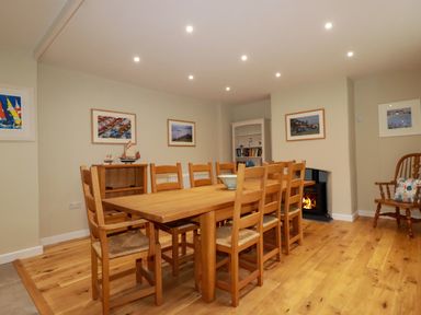 A dining room with a wooden table and chairs a fireplace and framed pictures on the walls at Tretoil Farm House in Bodmin
