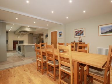 A dining area with a wooden table and chairs next to an open kitchen with island and cabinets at Tretoil Farm House Bodmin